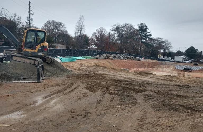 Excavator on gravel pile, site preparation, erosion control fence, land development.
