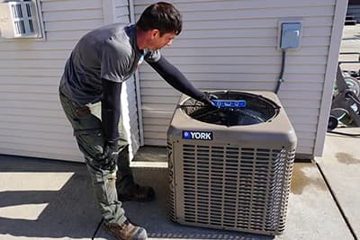 An air conditioning technician is finishing an install of a condenser by leveling it.
