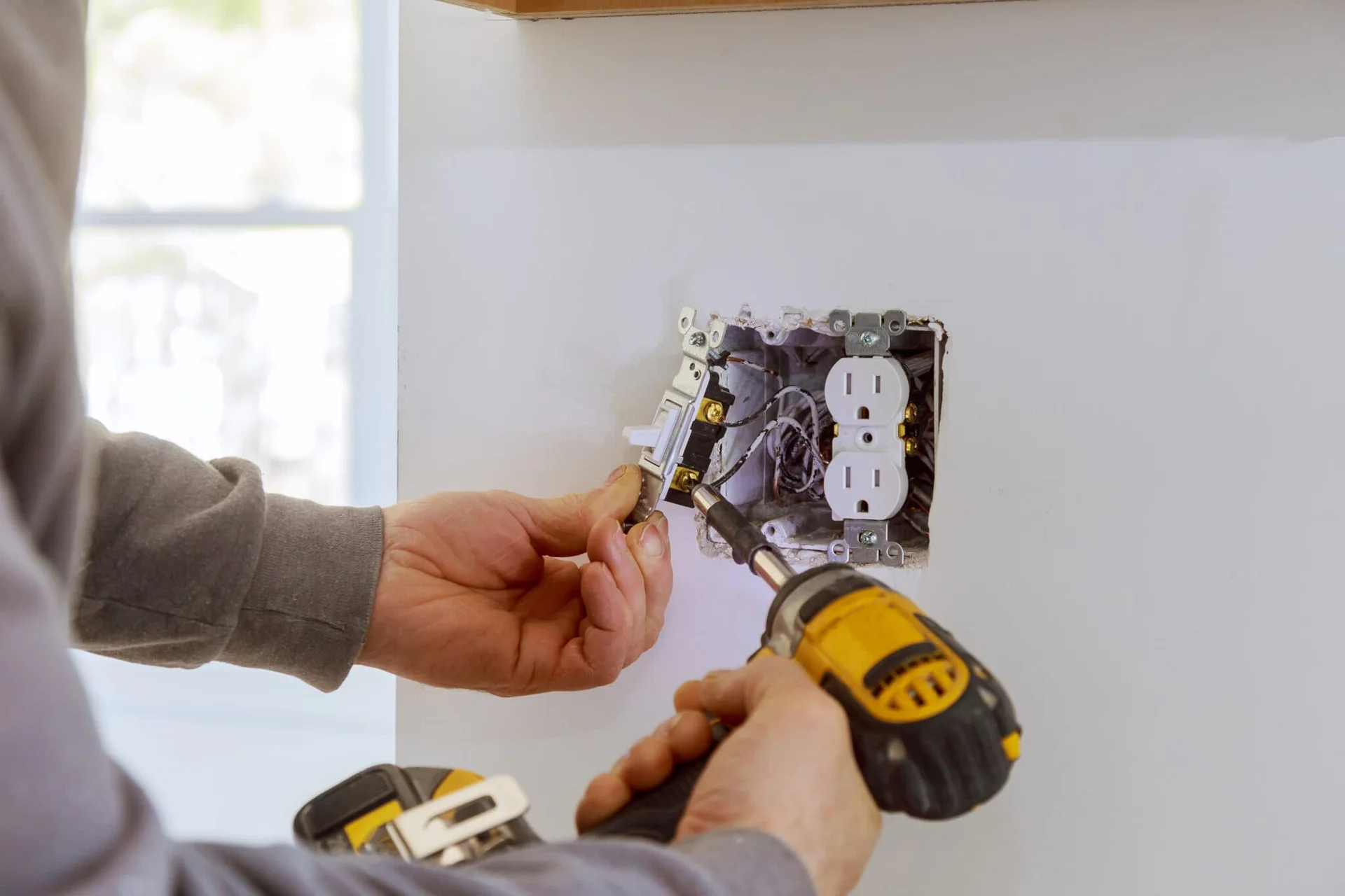 Person installing an electrical outlet with a drill and screwdriver.