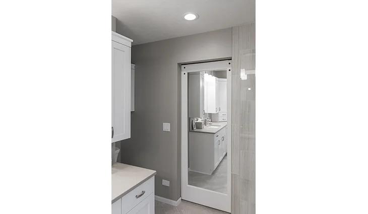 White cabinets with tan granite countertops and a white door with a mirror on the wall