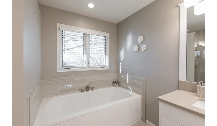 Newly renovated bathroom with a large white bathtub and a tan granite sink counter top