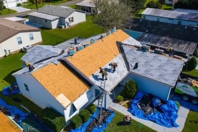 Roof installation in progress on residential home with workers and roofing materials.