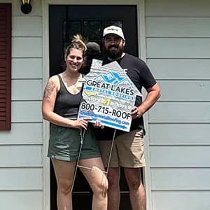 Two people standing in front of a house holding a for sale sign.