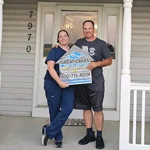 Two people standing on a porch holding a sign of Great Lakes Home Remodeling with a house in the background