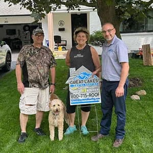 Three people standing on a front yard area with a tree, holding a Great Lakes Home Remodeling sign