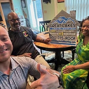 A salesman and two people sitting around a table with a Great Lakes Metal Roofing sign in the background.