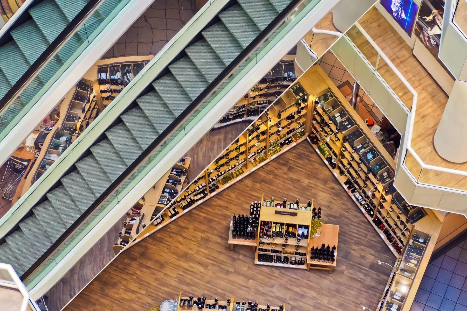 An overhead shot of a bar under escalators, demonstrating a rich, wooden coomercial flooring installation by Diverzify