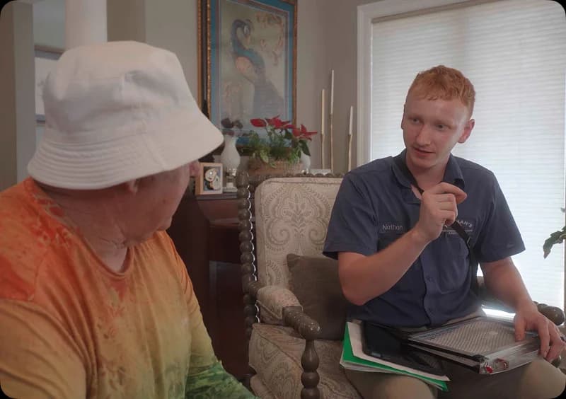 Technician discussing HVAC financing options with a customer in a cozy living room setting, featuring a clipboard and documents for reference.