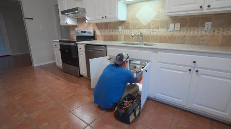 Plumber inspecting under kitchen sink for repairs in residential space, highlighting plumbing services in Gulfport, MS.