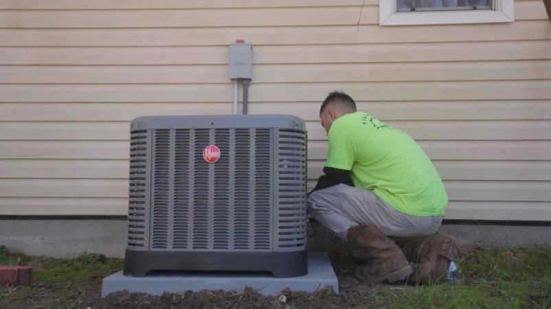 Technician in green shirt performing maintenance on a Rheem air conditioning unit outside a home, highlighting Tillman's Services' expertise in HVAC repair and installation in Gulfport, MS.