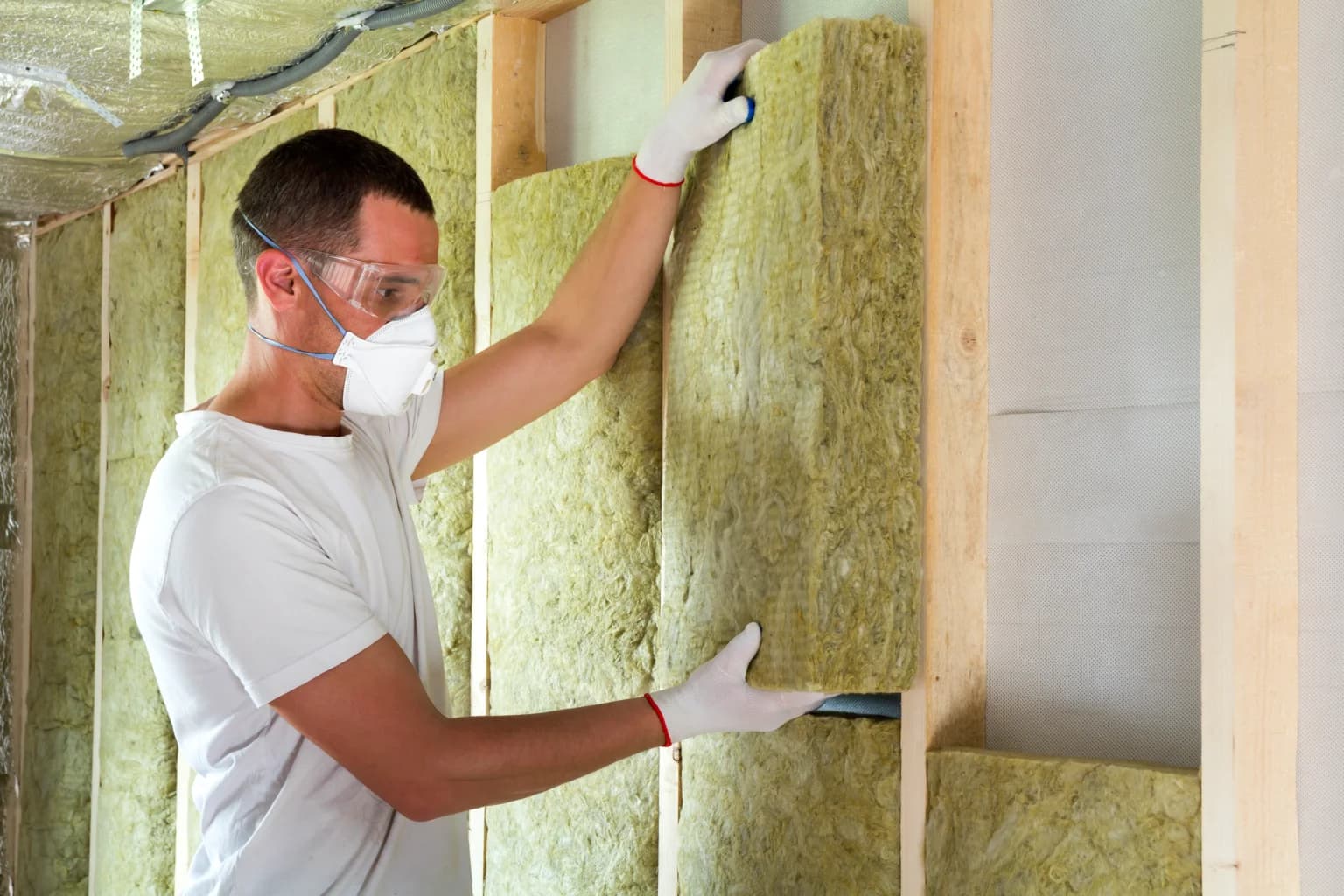 Worker in protective goggles and respirator insulating rock wool