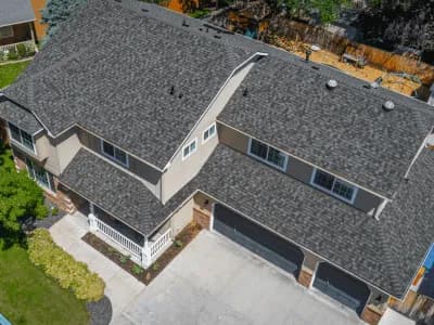 Aerial view of a tan two-story home with a bold, textured gray shingle roof and three-car black garage doors.