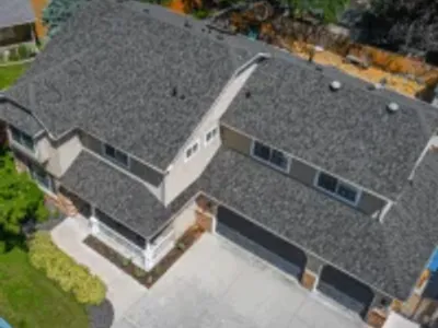 Aerial view of a tan two-story home with a bold, textured gray shingle roof and three-car black garage doors.