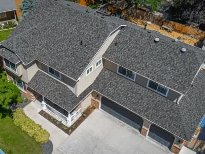 Aerial view of a tan two-story home with a bold, textured gray shingle roof and three-car black garage doors.