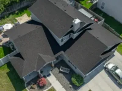 Overhead view of a large two-story home with a dark brown roof and tan siding, bordered by fencing and a tidy backyard.