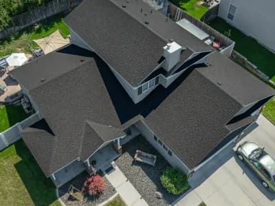 Overhead view of a large two-story home with a dark brown roof and tan siding, bordered by fencing and a tidy backyard.