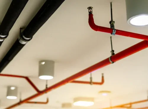Automatic fire sprinkler safety system and black water cooling supply pipe. Fire Suppression. Fire protection and detector. Fire sprinkler system with red pipes hanging from ceiling inside building.