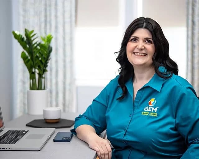 Female Gem Plumbing u0026amp; Heating employee sitting at a desk smiling