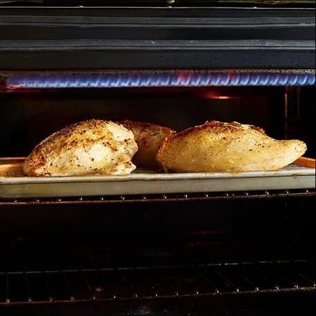 Seasoned chicken breast roasting on a sheet pan inside an oven.