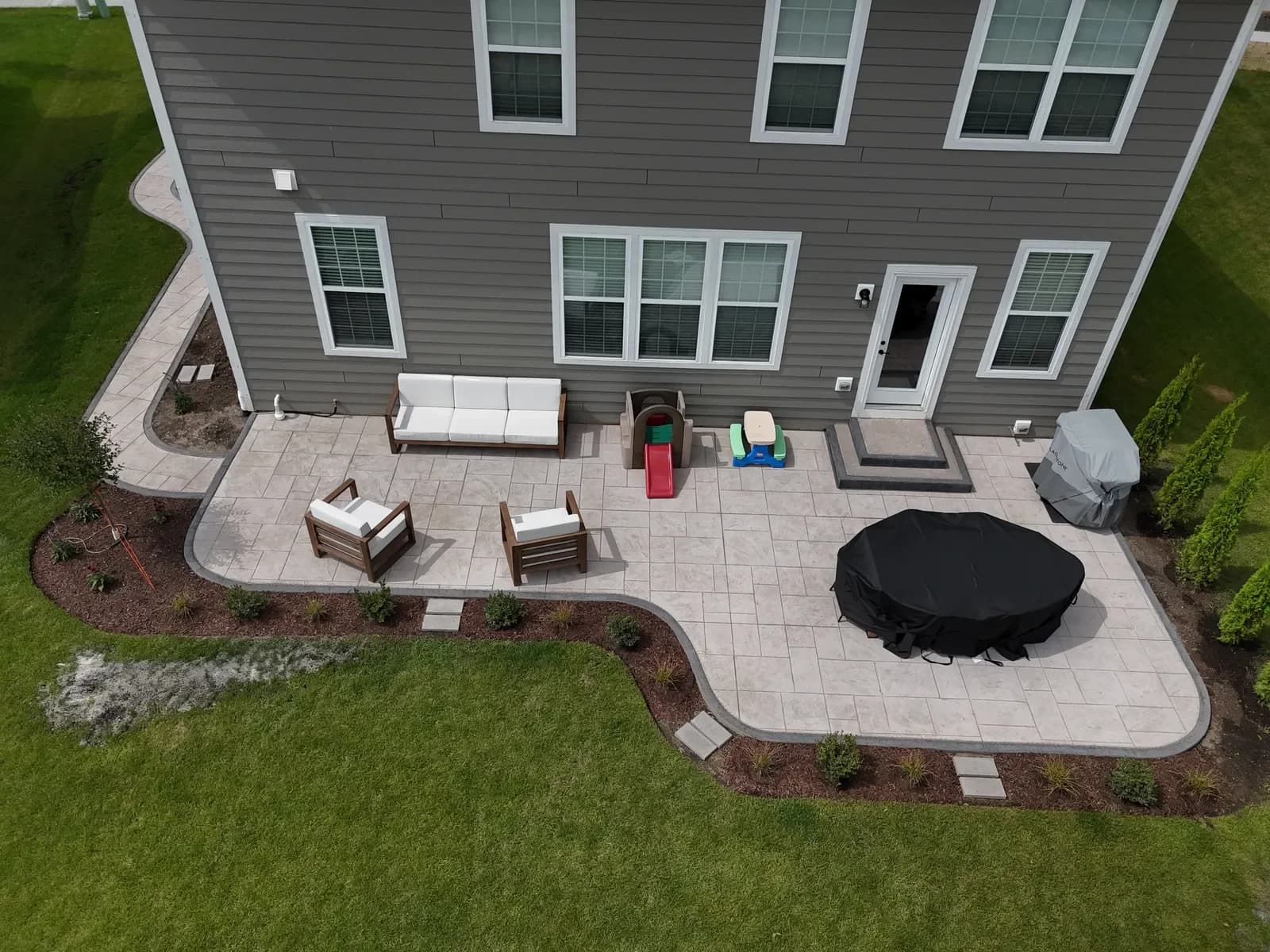 Stamped patio with fire pit and wraparound walkway — aerial
