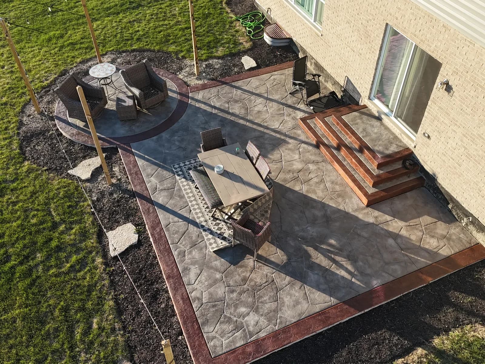 Stamped flagstone patio with fire pit circle — aerial drone view