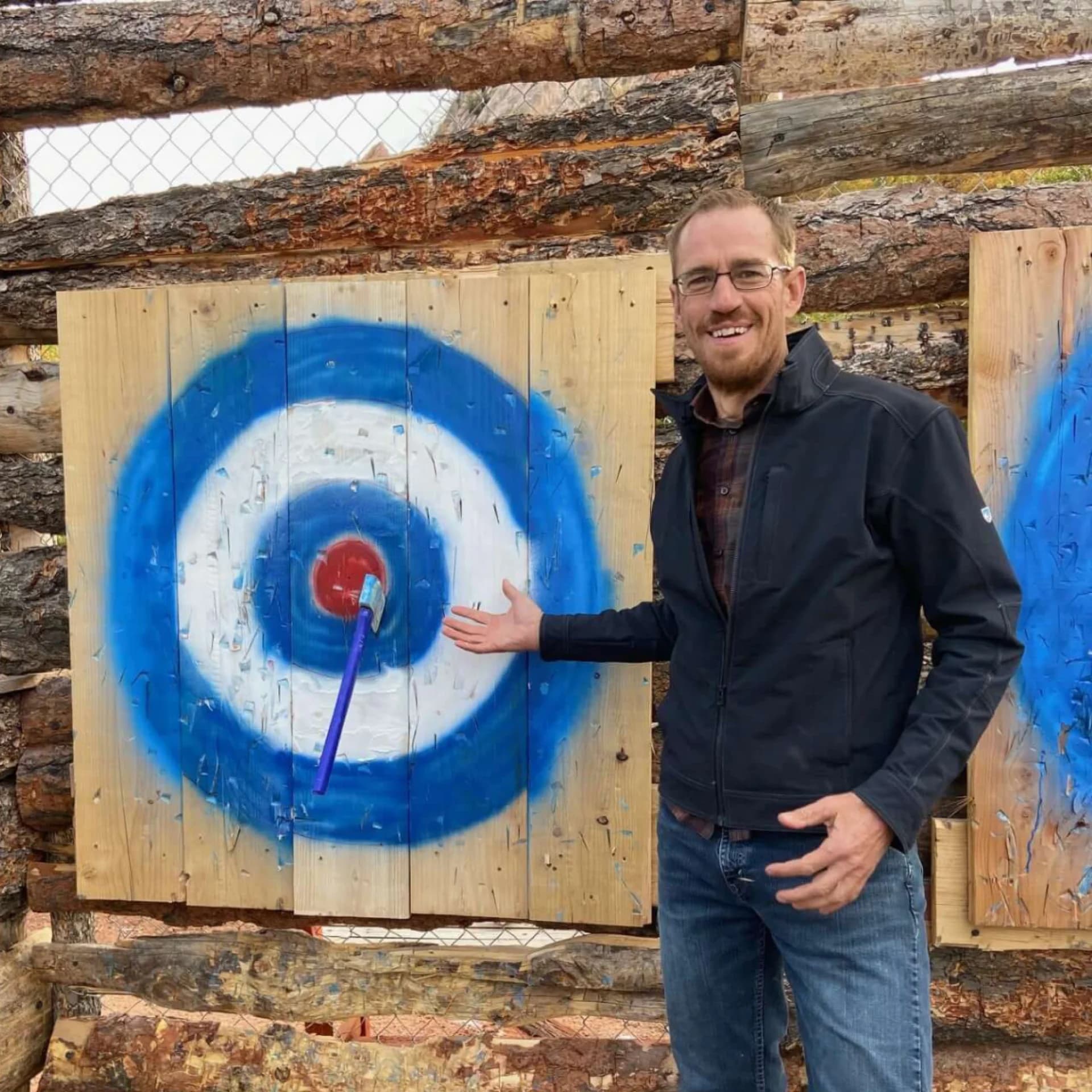 Man smiling and pointing at a target with a blue and red bullseye.