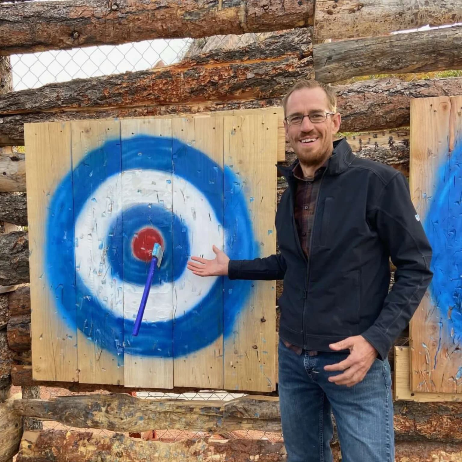 Man smiling and pointing at a target with a blue and red bullseye.