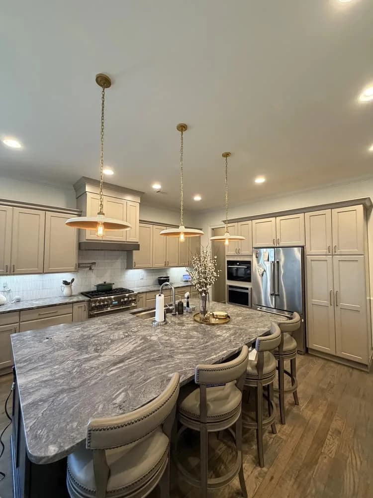 Luxury open kitchen and dining area with greige wainscoting, stone island, and brass chandelier pendants painted by OVO Painting in Atlanta