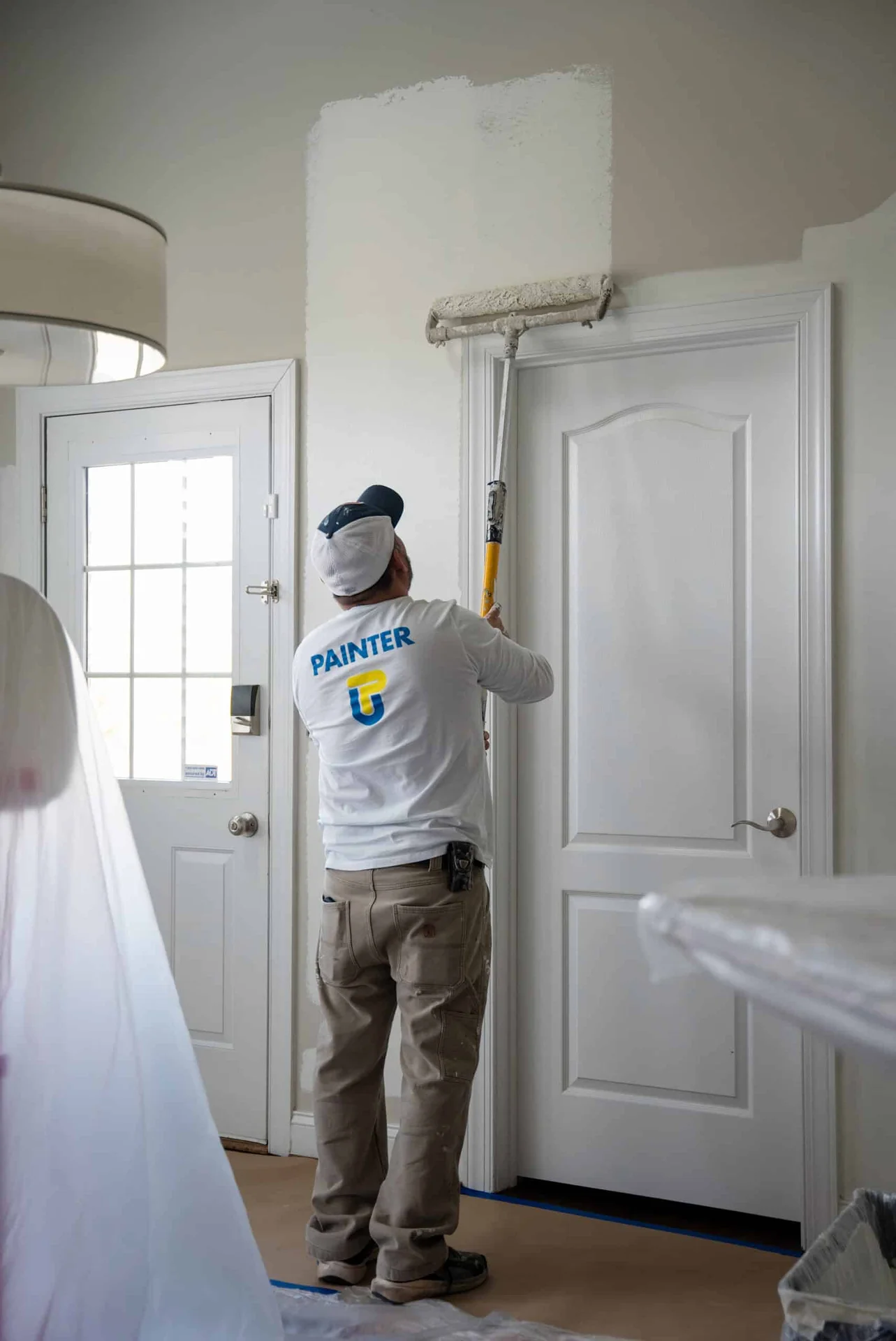 A professional painter applies fresh white paint to a residential interior wall above a door.