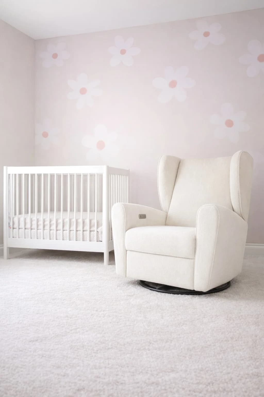 A cozy and bright nursery room with a white crib, cream rocking chair, and delicate floral wallpaper.