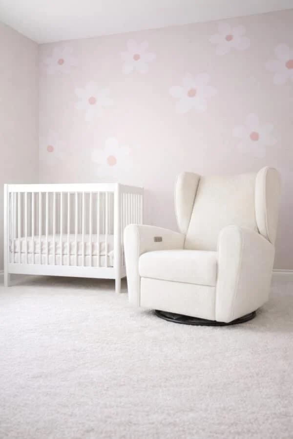 A cozy and bright nursery room with a white crib, cream rocking chair, and delicate floral wallpaper.