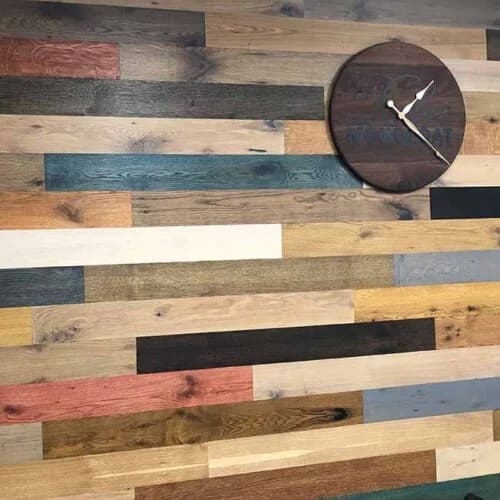 A wall adorned with a variety of colorful reclaimed wood planks, showcasing a rustic installation by Orange Cat Flooring in Atlanta, GA, with a wooden clock mounted on the wall.
