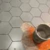 Hexagonal tiles being installed with precision by Orange Cat Flooring in Atlanta, GA, showing a close-up of the process with a bucket of mortar.