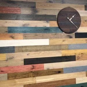 A wall adorned with a variety of colorful reclaimed wood planks, showcasing a rustic installation by Orange Cat Flooring in Atlanta, GA, with a wooden clock mounted on the wall.