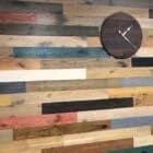 A wall adorned with a variety of colorful reclaimed wood planks, showcasing a rustic installation by Orange Cat Flooring in Atlanta, GA, with a wooden clock mounted on the wall.