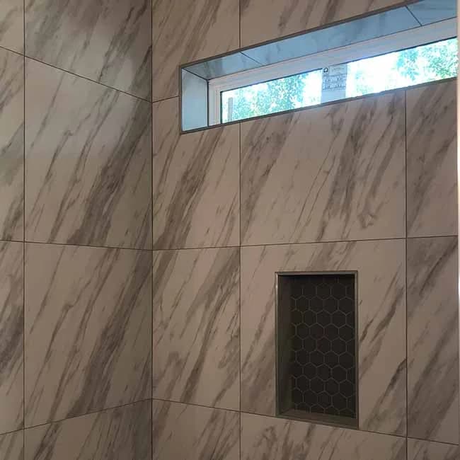 A beautifully tiled shower with large marble-pattern tiles and a built-in niche, installed by Orange Cat Flooring in Atlanta, GA.