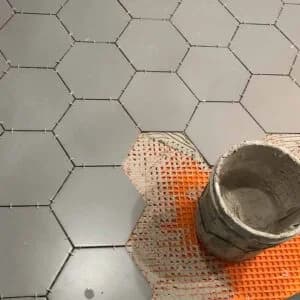 Hexagonal tiles being installed with precision by Orange Cat Flooring in Atlanta, GA, showing a close-up of the process with a bucket of mortar.