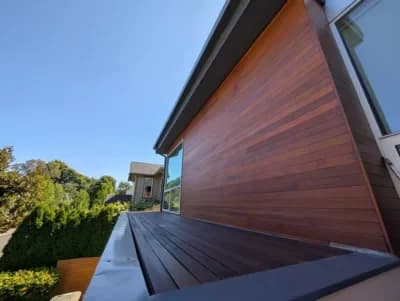 Modern house exterior featuring rich brown wood siding and a matching deck under a clear blue sky.