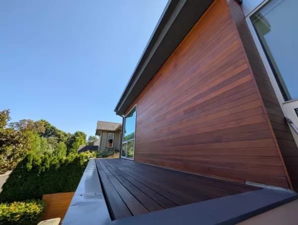 Modern house exterior featuring rich brown wood siding and a matching deck under a clear blue sky.