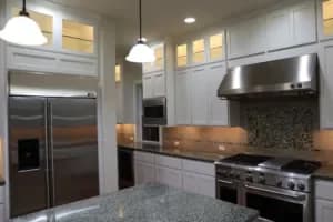 Upscale kitchen featuring elegant white painted cabinets, stainless steel appliances, and under cabinet lighting.
