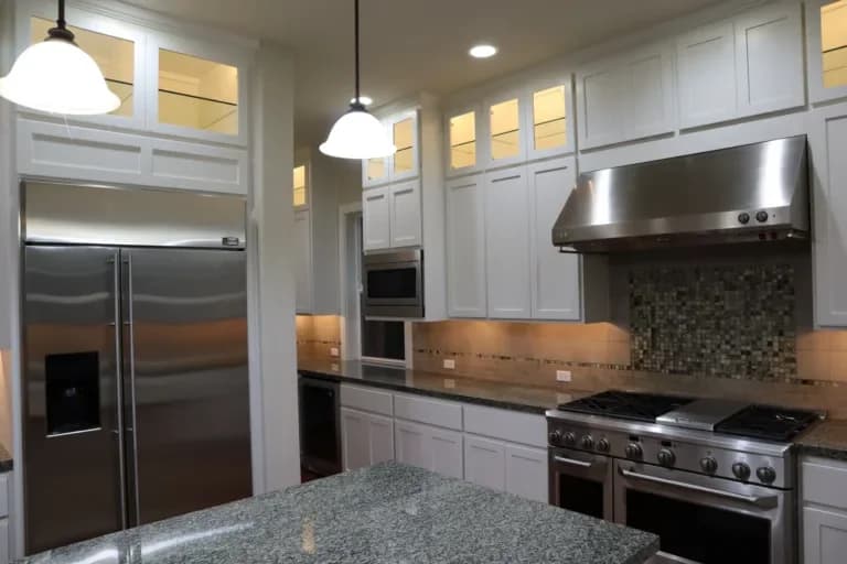 Upscale kitchen featuring elegant white painted cabinets, stainless steel appliances, and under cabinet lighting.