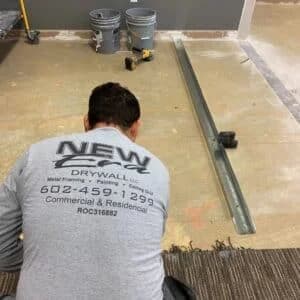 Phoenix Licensed and Bonded Drywall Installer wearing a New Era Drywall Company shirt prepares a floor for metal framing installation