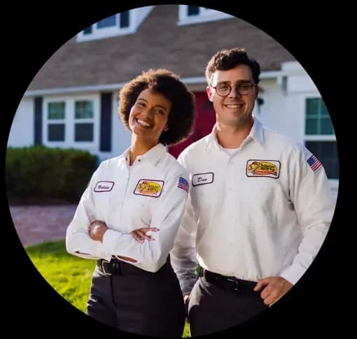 Two electricians in uniform smiling in front of a home.
