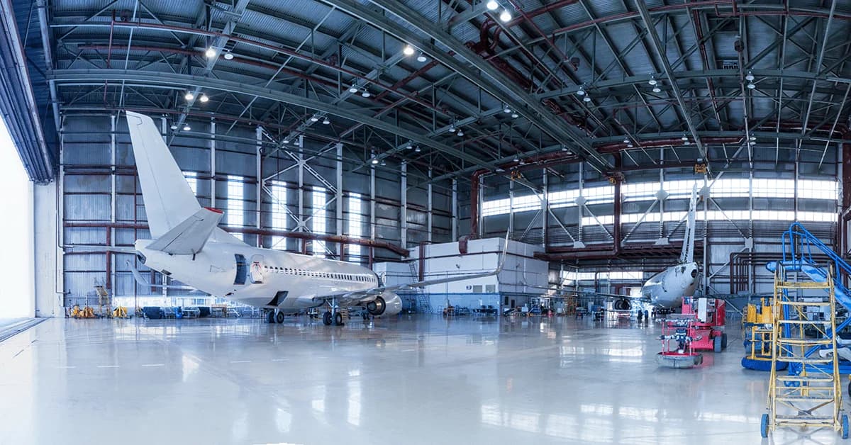 Interior of a large aviation maintenance hangar featuring a white private jet and maintenance equipment under a high-clearance ceiling.