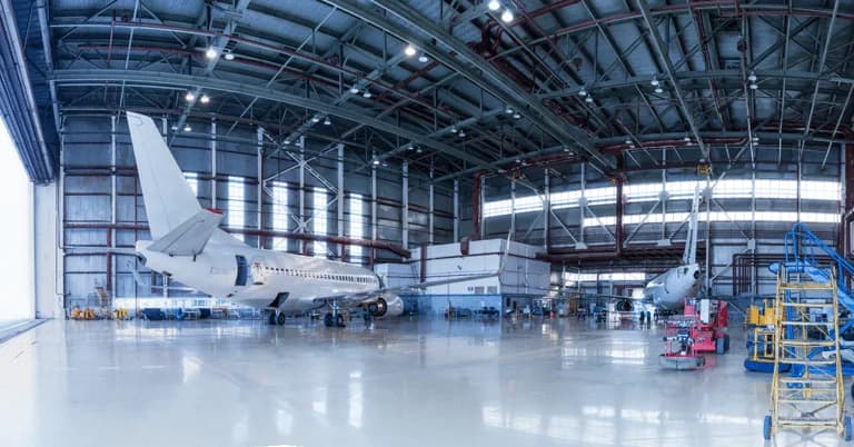 Interior of a large aviation maintenance hangar featuring a white private jet and maintenance equipment under a high-clearance ceiling.