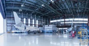 Interior of a large aviation maintenance hangar featuring a white private jet and maintenance equipment under a high-clearance ceiling.