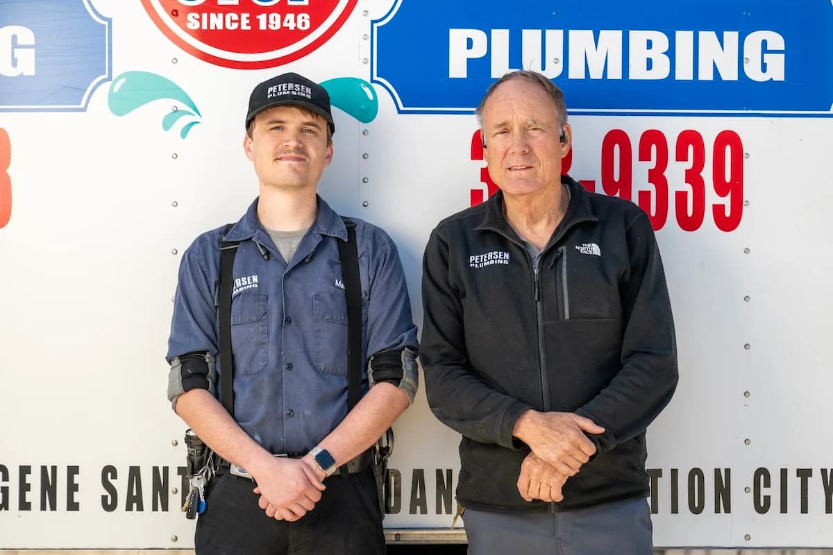 Two generations of Petersens standing in front of plumbing equipment.